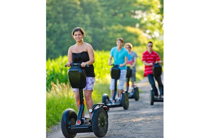 Vier Personen fahren auf Segways einen ländlichen Weg entlang, umgeben von grüner Natur und Bäumen im Hintergrund., © Cool-Tours StattReisen