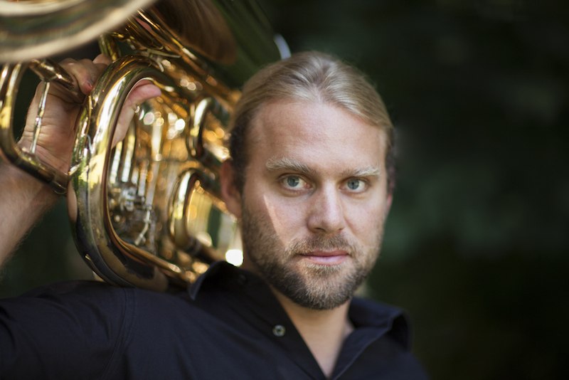 Ein Mann mit blonden Haaren und Bart h&auml;lt eine gl&auml;nzende Tuba auf der Schulter. Er tr&auml;gt ein schwarzes Hemd und blickt direkt in die Kamera., &copy; Rosenau Kultur e.V.