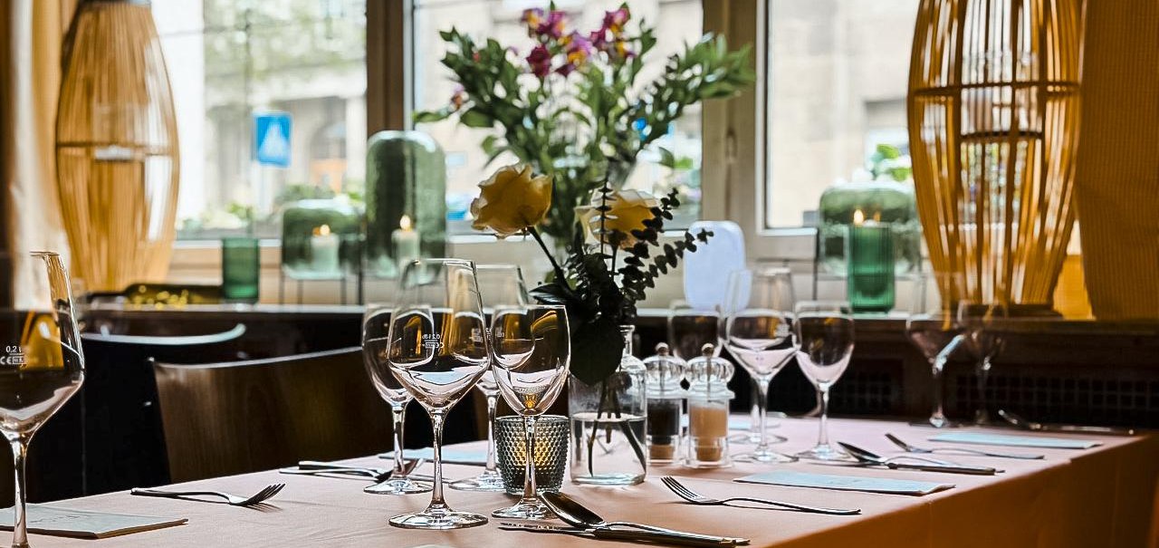 Ein elegant gedeckter Tisch in einem Café mit Weingläsern, Blumen und Kerzen, vor einem großen Fenster mit Blick nach draußen., © Cafe Stöckle FreCla, Stuttgart