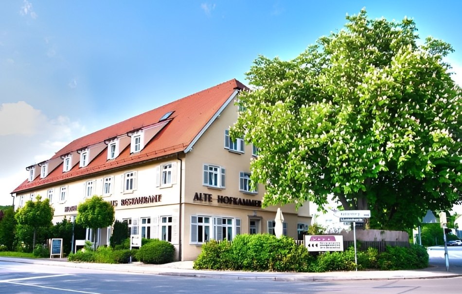 A hotel with a red roof and several windows, surrounded by trees and bushes, under a blue sky., © Hotel Neuwirtshaus A hotel with a red roof and several windows, surrounded by trees and bushes, under a blue sky., © Hotel Neuwirtshaus