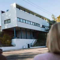 Two people look at the Le Corbusier house in the Wei&szlig;enhofsiedlung. Modern building with clear lines, surrounded by autumnal trees., &copy; Stuttgart-Marketing GmbH, wpsteinheisser