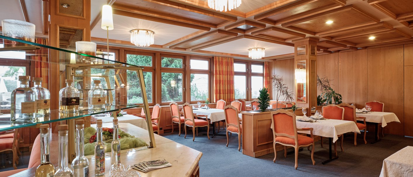 Elegantes Restaurant mit Holzeinrichtung, gedeckten Tischen und Kronleuchtern. Flaschen auf einer Theke, große Fenster mit Vorhängen., © Badhotel Restaurant Stauferland
