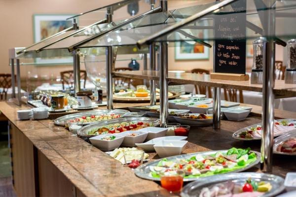 Ein Frühstücksbuffet mit einer Vielzahl von Speisen, darunter Obst, Gemüse, Käse und Aufschnitt, auf einem langen Tisch in einem Speisesaal., © Kronen Hotel GmbH Ein Frühstücksbuffet mit einer Vielzahl von Speisen, darunter Obst, Gemüse, Käse und Aufschnitt, auf einem langen Tisch in einem Speisesaal., © Kronen Hotel GmbH