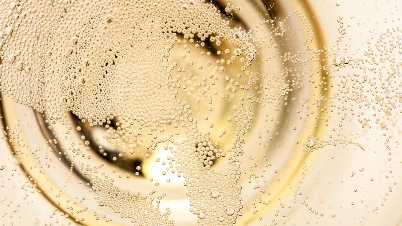 Nahaufnahme von vielen kleinen Champagnerblasen, die in einem Glas aufsteigen und ein schimmerndes Muster bilden., © unpict.com Nahaufnahme von vielen kleinen Champagnerblasen, die in einem Glas aufsteigen und ein schimmerndes Muster bilden., © unpict.com