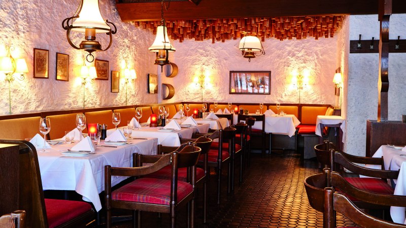 Cozy restaurant with wooden furniture, white tablecloths and warm lighting. The walls are rustic, decorated with pictures and lamps., © Steigenberger Graf Zeppelin Cozy restaurant with wooden furniture, white tablecloths and warm lighting. The walls are rustic, decorated with pictures and lamps., © Steigenberger Graf Zeppelin