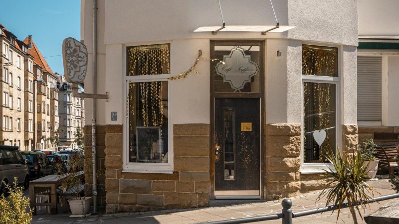 Eingang des Café Seyffer’s an einer Straßenecke, dekoriert mit goldenen Girlanden und Pflanzen. Die Straße ist von Wohnhäusern gesäumt., © SMG, Sarah Schmid