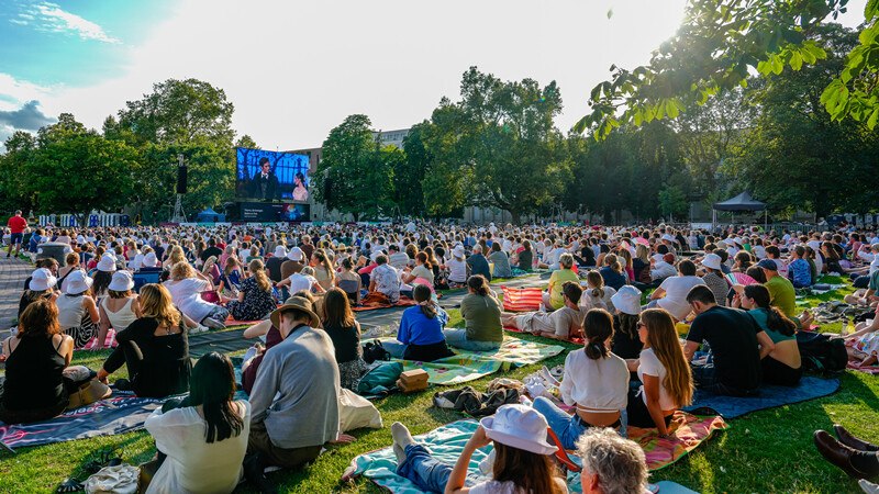 Many people sit on blankets in the park and watch a big screen. The atmosphere is relaxed and summery., © Württembergische Staatstheater Stuttgart Many people sit on blankets in the park and watch a big screen. The atmosphere is relaxed and summery., © Württembergische Staatstheater Stuttgart