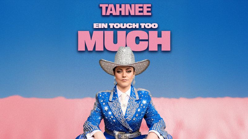 Eine Person in einem glitzernden blauen Cowboy-Outfit sitzt vor einem blauen Hintergrund. Dar&uuml;ber steht der Text 'TAHNEE - EIN TOUCH TOO MUCH'., &copy; links im Bild