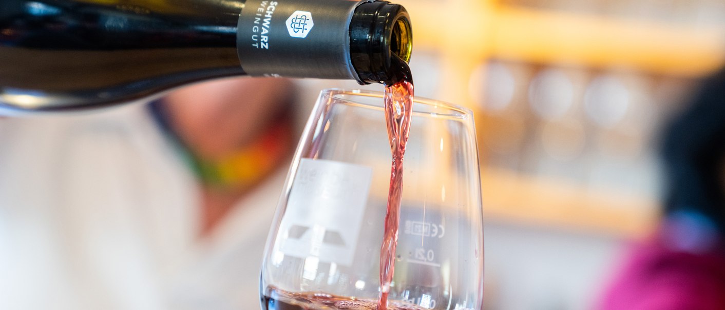 A wine bottle pours red wine into a glass. The background is blurred, the focus is on the flowing wine., © Thomas Niedermüller A wine bottle pours red wine into a glass. The background is blurred, the focus is on the flowing wine., © Thomas Niedermüller