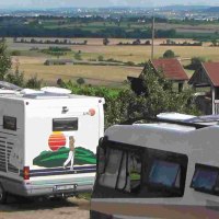 RV campers are parked in a campsite overlooking a vast landscape and fields. In the background, you can see hills and a town., &copy; PANORAMAWEINGUT Baumg&auml;rtner