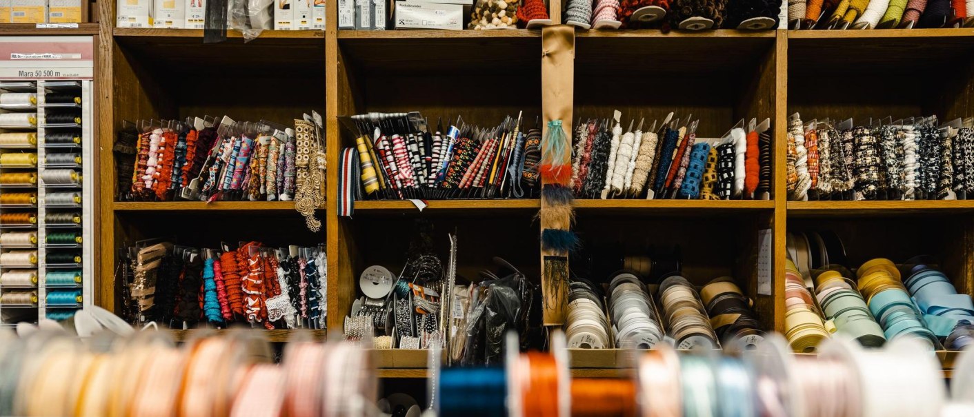 Ein Regal voller bunter Bänder und Garnrollen in einem Nähgeschäft. Verschiedene Farben und Muster sind ordentlich sortiert., © Stuttgart-Marketing GmbH, Sarah Schmid