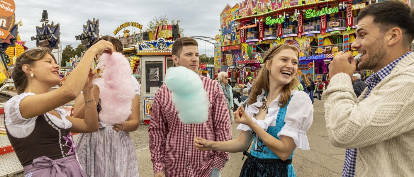 People in traditional costume enjoy candy floss at a colorful folk festival in Stuttgart. Rides and colorful lights can be seen in the background., &copy; Stuttgart-Marketing GmbH, Sarah Schmid