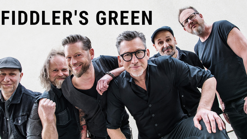 Die Band Fiddler's Green posiert fr&ouml;hlich f&uuml;r ein Gruppenfoto. Sechs Mitglieder stehen nebeneinander vor einem hellen Hintergrund., &copy; links im Bild