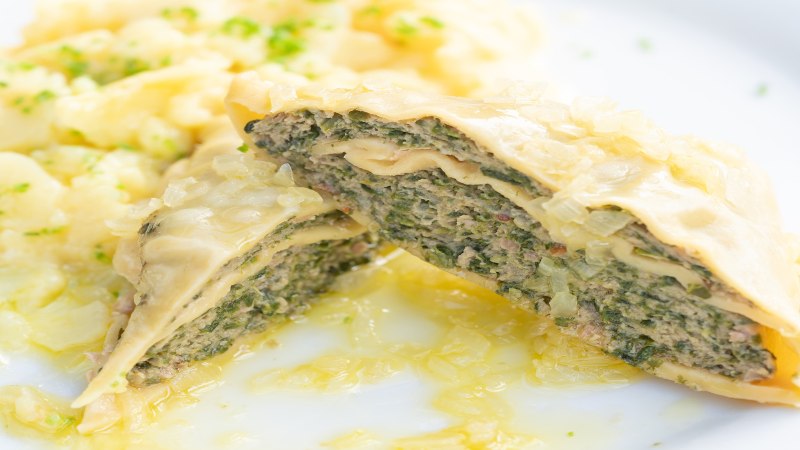 Close-up of Maultaschen with a filling of meat and herbs, served with potato salad on a white plate., © Herr Kächele - Schwäbisches für Schleckige GmbH