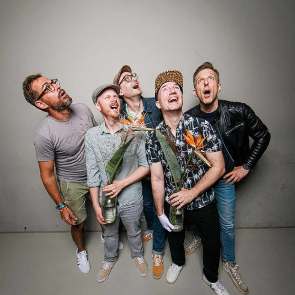 Fünf Männer blicken überrascht nach oben. Zwei von ihnen halten Blumensträuße. Sie tragen lässige Kleidung und wirken fröhlich., © Peerplex Fünf Männer blicken überrascht nach oben. Zwei von ihnen halten Blumensträuße. Sie tragen lässige Kleidung und wirken fröhlich., © Peerplex