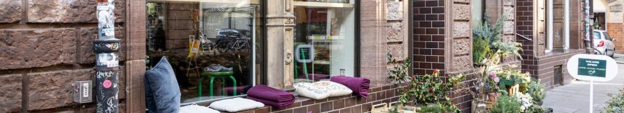 A cozy caf&eacute; with plants and cushions on the windowsill. A sign advertises coffee and cookies. The fa&ccedil;ade is made of brown bricks., &copy; Stuttgart-Marketing GmbH, Sarah Schmid