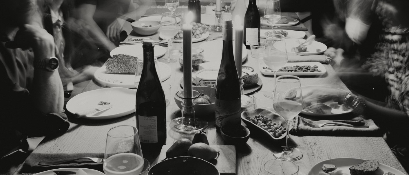 Ein Esstisch mit Kerzen, Weinflaschen und Tellern. Menschen sitzen um den Tisch, die Szene ist in Schwarz-Wei&szlig; gehalten., &copy; Peter Oliver Wolff / DAS EDITH