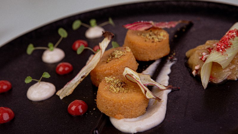 Gourmet dish on a black plate, decorated with sauces, herbs and vegetables. Elegant arrangement with different textures and colors., © Marc Luppa