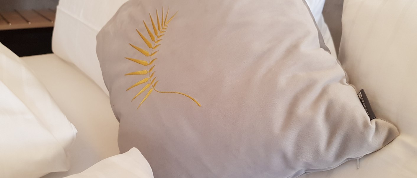 Ein Bett mit weißen Kissen und einem grauen Zierkissen mit gelbem Blattmuster., © ©hotel-graf-eberhard.de