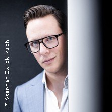 Ein Mann mit Brille und Anzug schaut hinter einer Wand hervor. Er tr&auml;gt ein helles Hemd und hat dunkles Haar., &copy; links im Bild