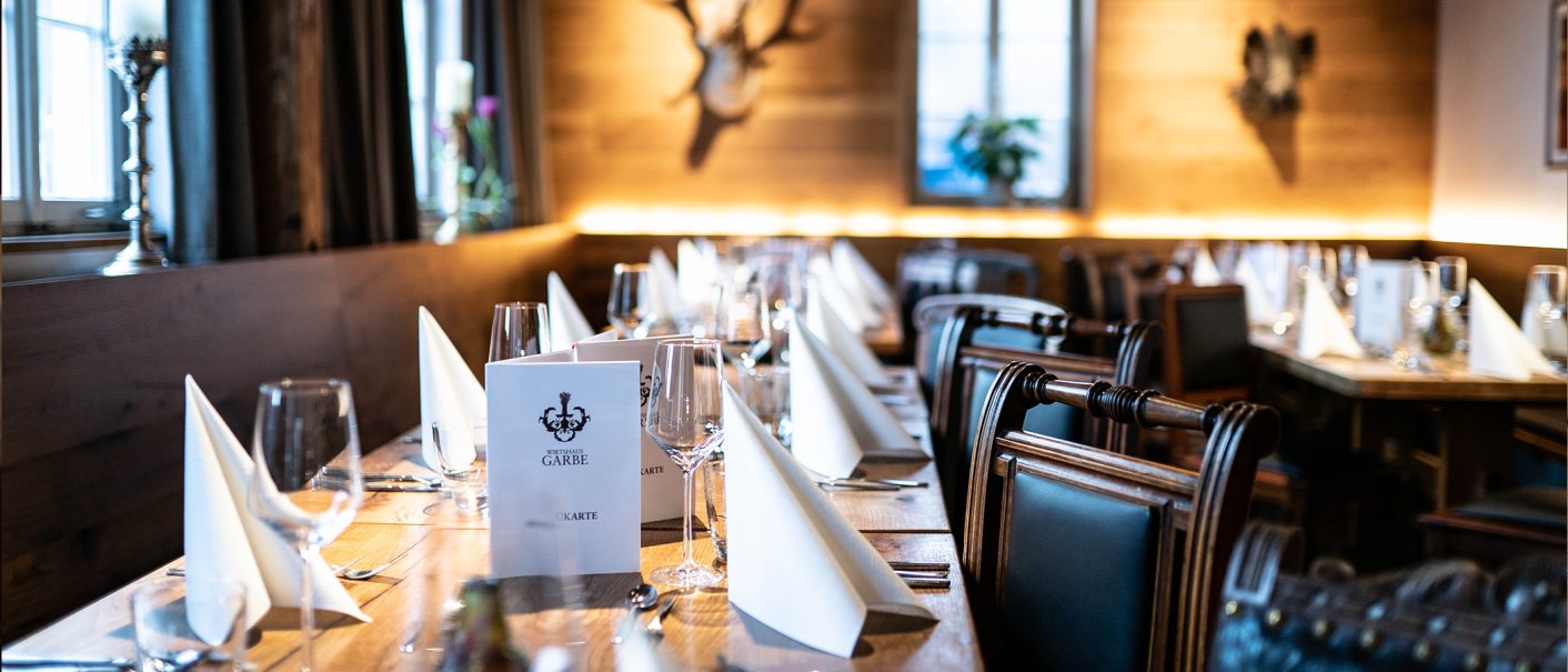 Elegant restaurant with table setting, white napkins and wine glasses, wooden walls and antler decorations., © Cara Schmid