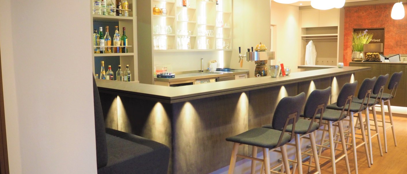 A modern bar with high stools, an illuminated counter and shelves full of bottles. The lighting is warm and inviting., © TOMAS A modern bar with high stools, an illuminated counter and shelves full of bottles. The lighting is warm and inviting., © TOMAS