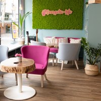Bright caf&eacute; with modern gray and pink chairs, wooden tables and green plants. Large window front and green moss wall with "Energetic life" lettering., &copy; � 2022 Anastasiia Vovk, all rights reserved.