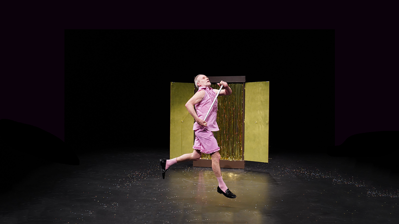 Person in a pink outfit dances on a stage in front of golden curtains. The floor is covered in glitter., &copy; W&uuml;rttembergische Staatstheater Stuttgart