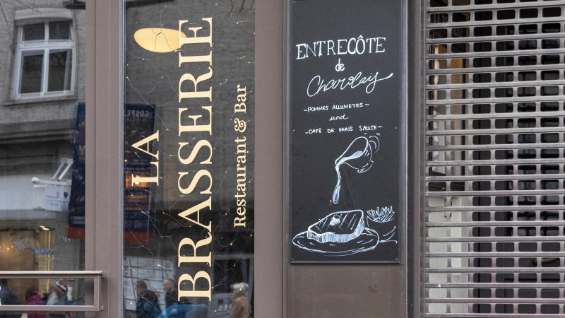 Eingang von 'La Brasserie' mit Men&uuml;tafel, die Entrec&ocirc;te de Charolais mit Pommes und Caf&eacute; de Paris Sauce anbietet., &copy; SMG, Sarah Schmid