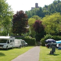 Campingplatz mit Wohnmobilen und Zelten, umgeben von grünen Bäumen und Hügeln. Im Hintergrund ist eine Burg auf einem Hügel zu sehen., © Campingpark Bad Liebenzell, Andreas Harter