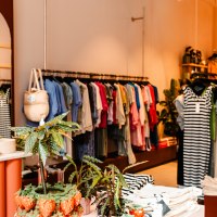 A clothing store with colorful clothes on clothes rails, plants and a mirror in the background., © Sarah Schmid A clothing store with colorful clothes on clothes rails, plants and a mirror in the background., © Sarah Schmid