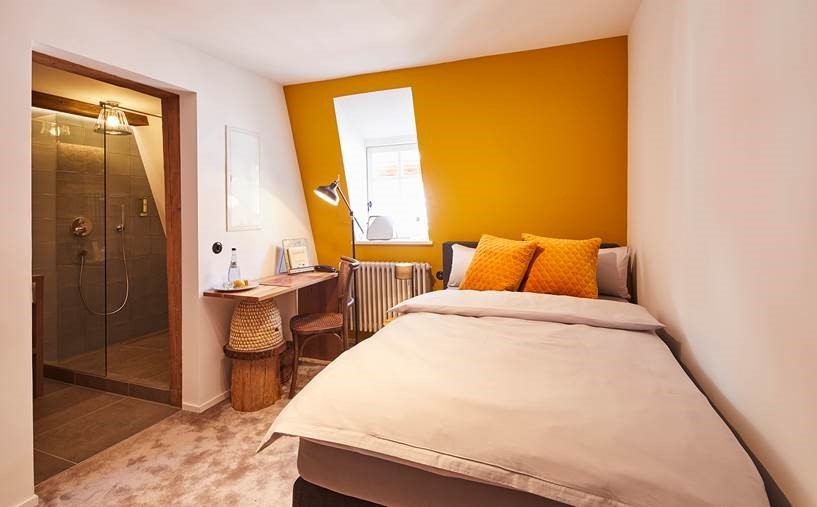 Kleines Schlafzimmer mit gelber Akzentwand, Einzelbett, Schreibtisch und angrenzendem Badezimmer mit Dusche. Helle und gem&uuml;tliche Atmosph&auml;re., &copy; Hotel Restaurant Bachofer