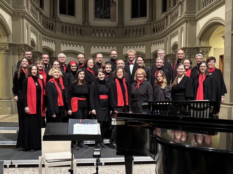 Der Junger Chor Stuttgart posiert in der Matthäuskirche. Die Mitglieder tragen schwarze Kleidung mit roten Schals und Accessoires., © Junger Chor Stuttgart e.V.