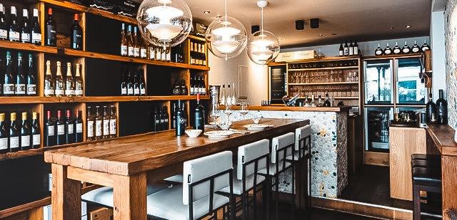 Stilvolle Weinbar mit Holztischen, hohen Stühlen und Weinregalen. Moderne Beleuchtung und gemütliche Atmosphäre., © Stadtbesen!