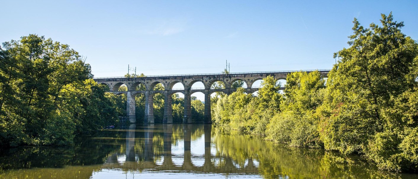 A viaduct spans a river, surrounded by green trees and a clear sky. The bridge is reflected in the water., © SMG Stuttgart Marketing GmbH - Sarah Schmid A viaduct spans a river, surrounded by green trees and a clear sky. The bridge is reflected in the water., © SMG Stuttgart Marketing GmbH - Sarah Schmid