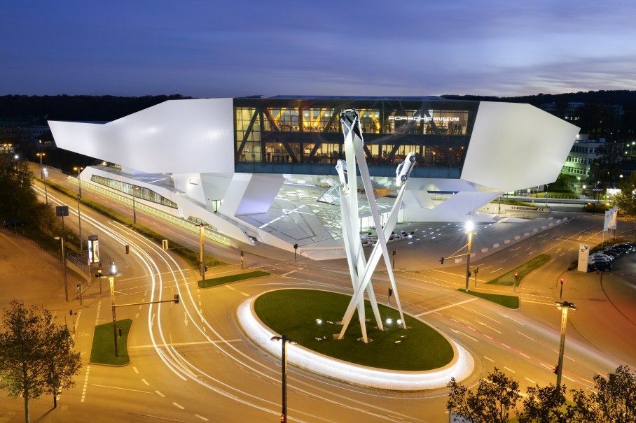 The Porsche Museum at night, illuminated with modern architecture and a sculpture of three cars on high pillars., © Porsche Museum The Porsche Museum at night, illuminated with modern architecture and a sculpture of three cars on high pillars., © Porsche Museum