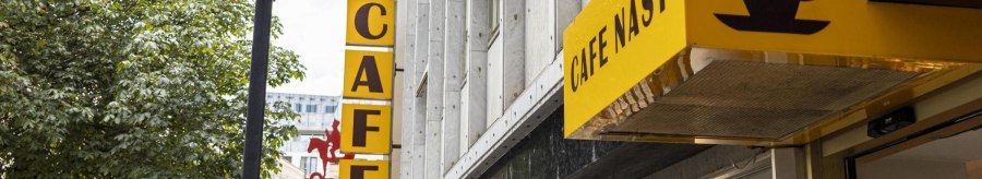 Yellow Cafe Nast sign with coffee cup logo on a building surrounded by trees., &copy; SMG, Sarah Schmid