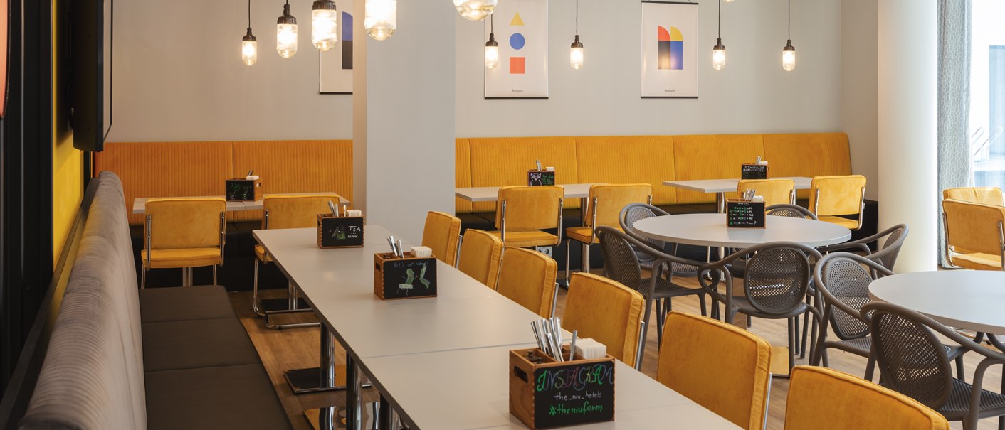 A modern restaurant with yellow chairs, tables, and hanging lamps. Abstract artwork on the walls creates a stylish atmosphere., © the niu Form - Novum Hospitality A modern restaurant with yellow chairs, tables, and hanging lamps. Abstract artwork on the walls creates a stylish atmosphere., © the niu Form - Novum Hospitality