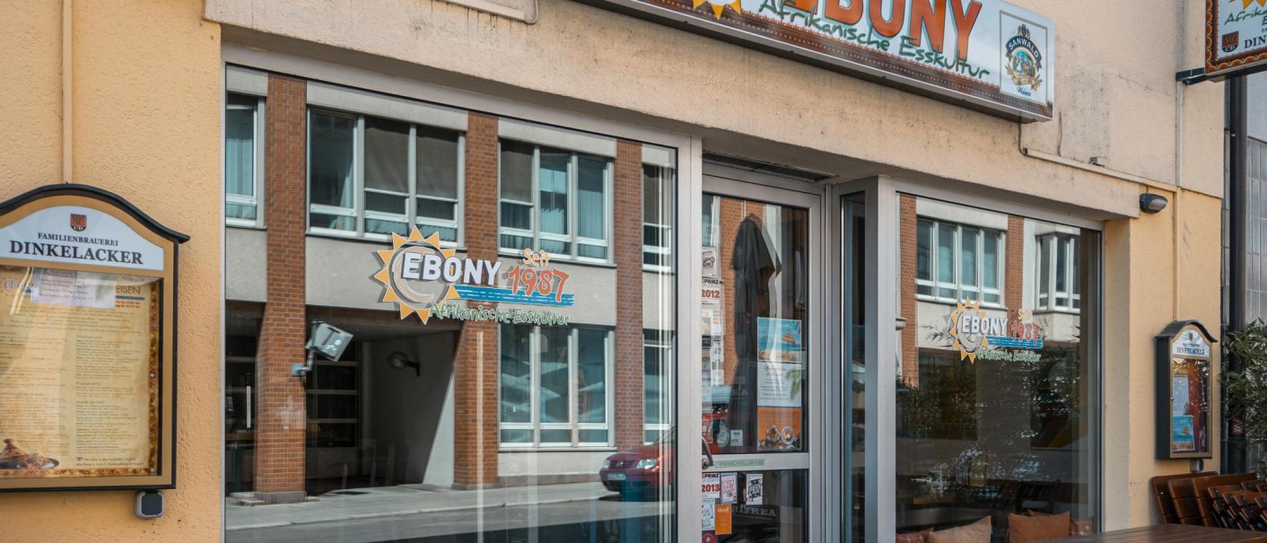 Eingang des Restaurants 'Ebony' mit Schildern für afrikanische Küche. Fenster spiegeln die gegenüberliegende Straße wider. Seit 1987 geöffnet., © SMG, Sarah Schmid