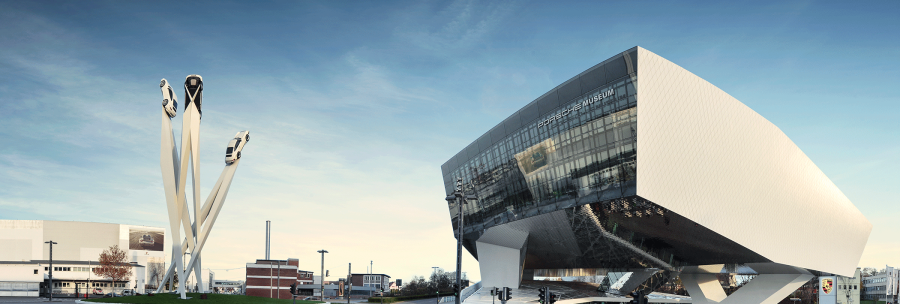 The Porsche Museum in Stuttgart with its futuristic architecture and a sculpture of three cars on tall pillars against a blue sky., &copy; Porsche AG