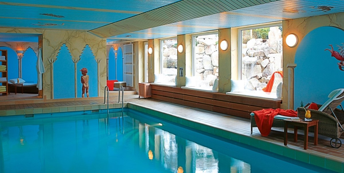 Elegant indoor pool with blue walls, sun loungers and large windows. Decorative elements and cozy atmosphere., © Hotel Azenberg GmbH/Stefan Ott Elegant indoor pool with blue walls, sun loungers and large windows. Decorative elements and cozy atmosphere., © Hotel Azenberg GmbH/Stefan Ott