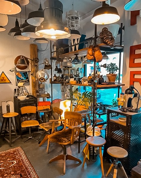 Ein Raum mit Vintage-Möbeln, Lampen und Dekorationen. Boxhandschuhe hängen an einem Regal. Verschiedene Stühle und Pflanzen sind zu sehen., © Dr. Bohne, Stuttgart