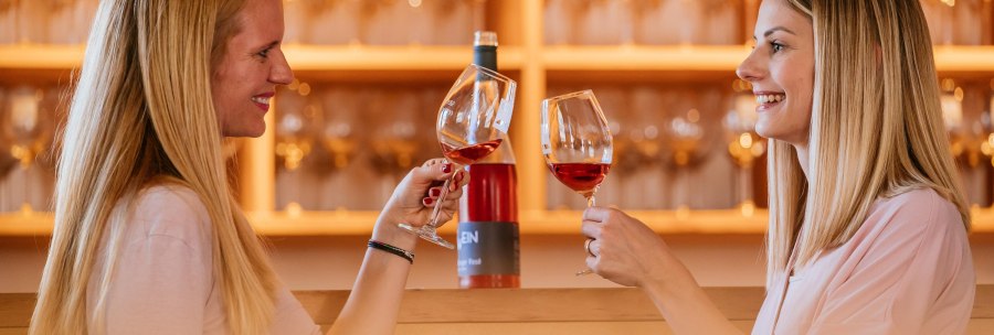 Zwei Frauen sto&szlig;en mit Weingl&auml;sern in einer Vinothek an. Im Hintergrund sind Weinflaschen und Gl&auml;ser zu sehen., &copy; Stuttgart-Marketing GmbH, Thomas Niederm&uuml;ller