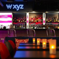 Moderne Bar mit Neon-Schriftzug 'W XYZ', beleuchtetem Tresen und gemütlicher Atmosphäre. Kerzen auf den Tischen sorgen für stimmungsvolles Licht., © Aloft Stuttgart