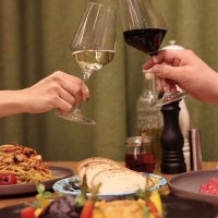 Two people toast with glasses of white and red wine, surrounded by pasta, bread and vegetable dishes on a table., &copy; Roberts