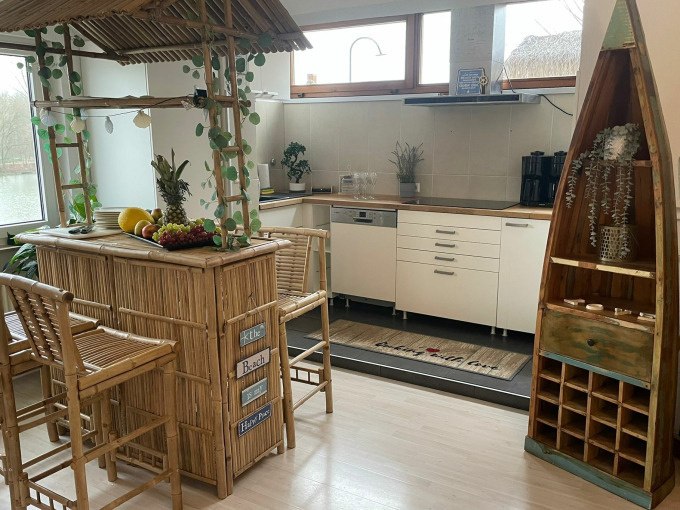 Bright kitchen with bamboo bar, decorated with fruit and plants. A boat-shaped shelf on the right, window with a view of the water in the background., © Cool-Tours StattReisen Bright kitchen with bamboo bar, decorated with fruit and plants. A boat-shaped shelf on the right, window with a view of the water in the background., © Cool-Tours StattReisen