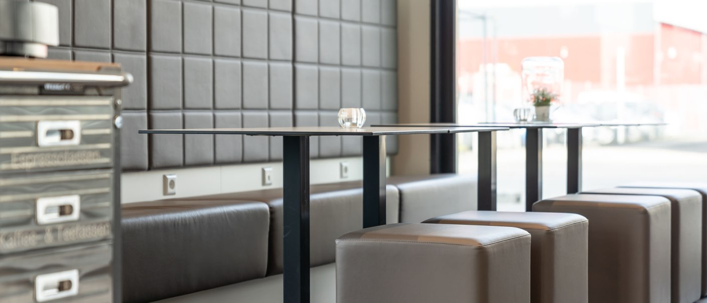 Modern breakfast area with upholstered benches, cube stools and a table. In the background is a window with a view outside., © a2 HOTELS Modern breakfast area with upholstered benches, cube stools and a table. In the background is a window with a view outside., © a2 HOTELS