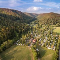Luftaufnahme des Campingplatzes Pfählhof in einem bewaldeten Tal mit Wohnwagen und Zelten, umgeben von Hügeln und einer Straße., © Campingplatz Pfählhof