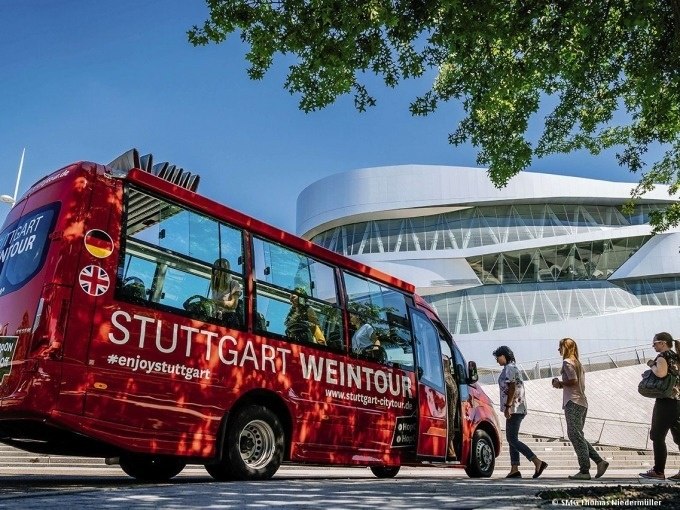 Roter Bus der 'Stuttgart Weintour' vor dem modernen Mercedes-Benz Museum in Stuttgart, umgeben von Passanten und Bäumen., © SMG, Thomas Niedermüller Roter Bus der 'Stuttgart Weintour' vor dem modernen Mercedes-Benz Museum in Stuttgart, umgeben von Passanten und Bäumen., © SMG, Thomas Niedermüller