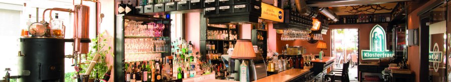 Bar mit Flaschen, Gläsern und Kupferdestille. Klosterfrau-Logo leuchtet im Hintergrund. Gemütliche Atmosphäre mit Holzmöbeln und Lampen., © Buschwerk Mediendesign-Wilhelmer Gastronomie